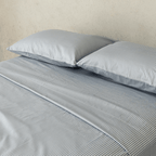 Close-up of two gray and white striped pillows resting on matching striped sheets, highlighting the fine vertical pattern and smooth finish.