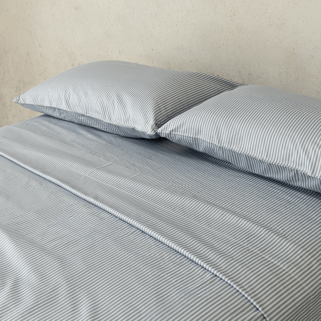 Close-up of two gray and white striped pillows resting on matching striped sheets, highlighting the fine vertical pattern and smooth finish.
