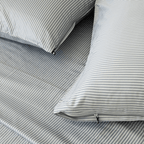 Close-up of gray and white striped pillowcases with concealed zipper closures and small black zipper pulls on matching bedding.