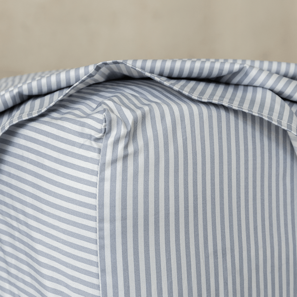 Close-up of a gray and white striped fitted sheet stretched over a mattress corner, showing the stitched seam and snug fit.
