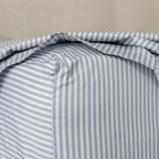 Close-up of a gray and white striped fitted sheet stretched over a mattress corner, showing the stitched seam and snug fit.