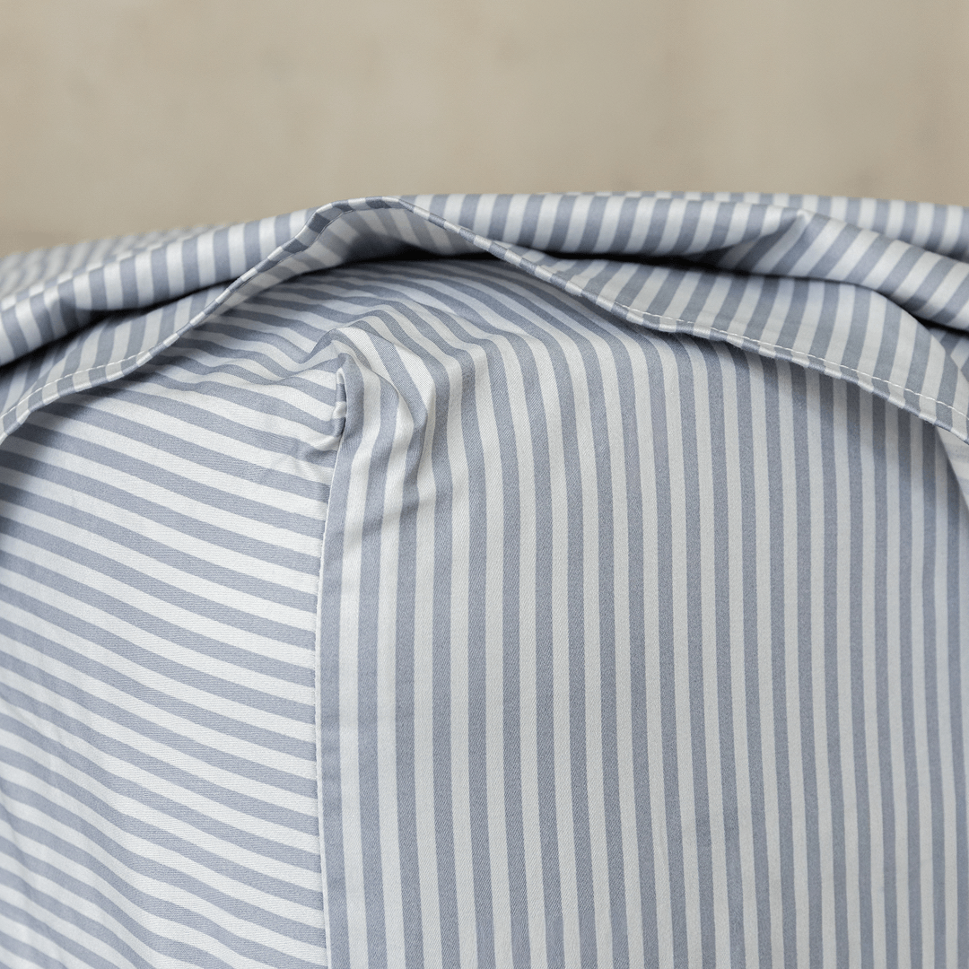 Close-up of a gray and white striped fitted sheet stretched over a mattress corner, showing the stitched seam and snug fit.