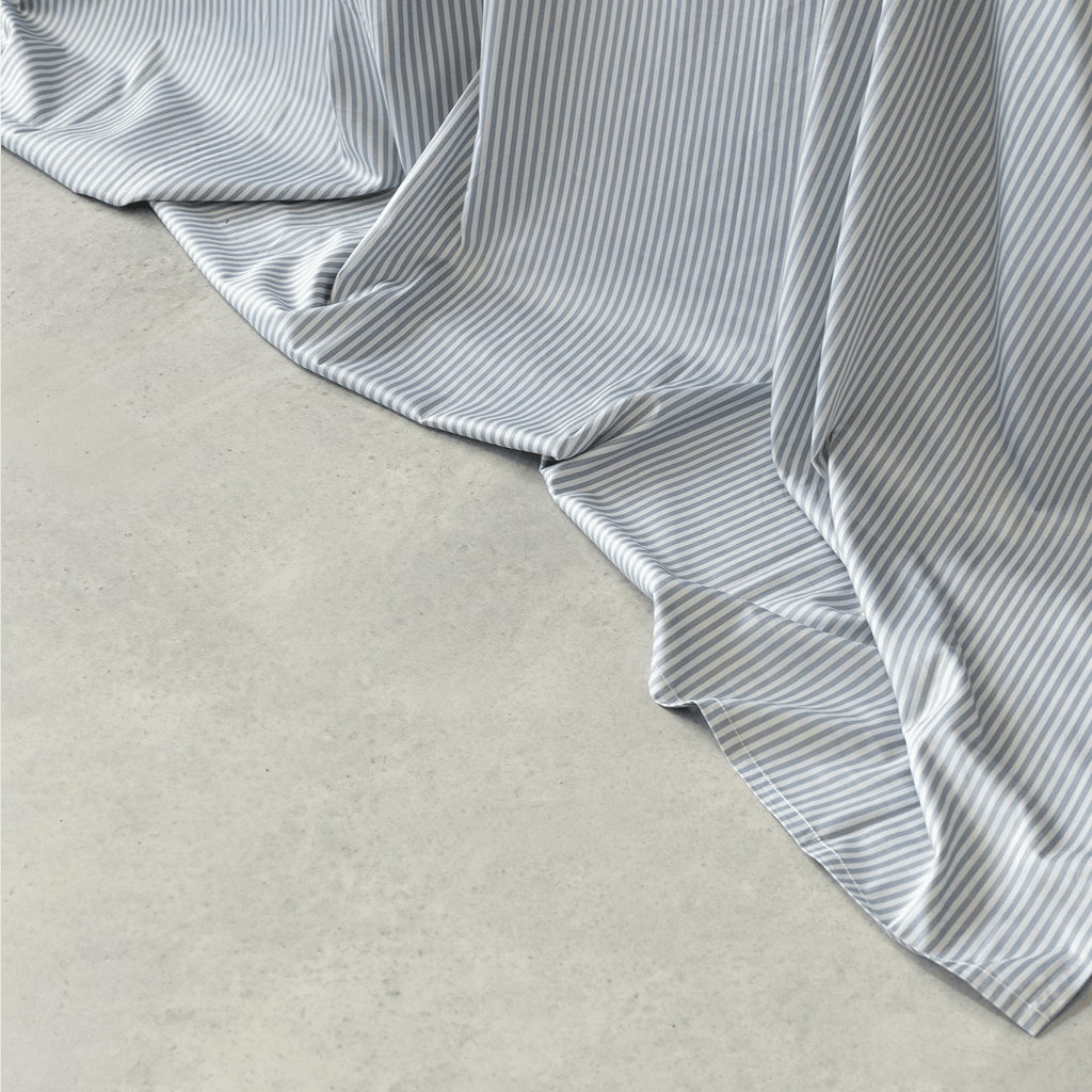 Close-up of a gray and white striped flat sheet draping softly onto a concrete floor, showing its smooth texture and flowing folds.