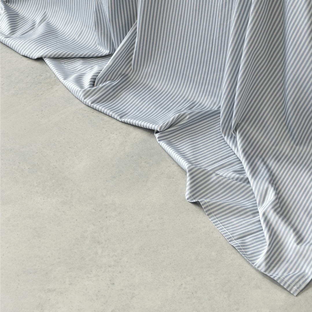 Close-up of a gray and white striped flat sheet draping softly onto a concrete floor, showing its smooth texture and flowing folds.