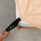 Hand pulling the fitted sheet labelled corner loop strap onto the mattress.  