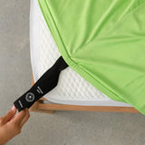 Close up of our lime green fitted sheet with the labelled corner loop strap that says 'Bottom Left' and 'Double', being pulled onto a bed corner by a hand.
