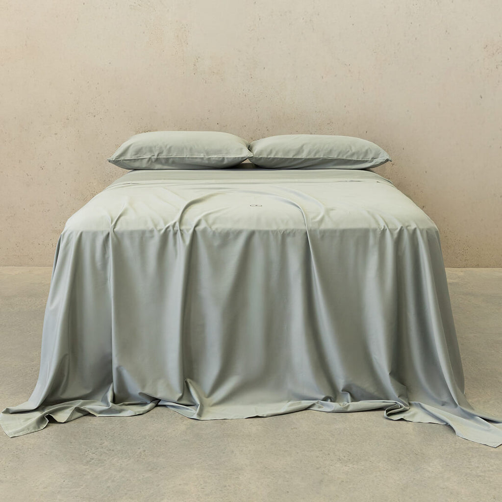 Light grey bedspread and pillows on a bed against a beige wall.