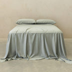 Light grey bedspread and pillows on a bed against a beige wall.