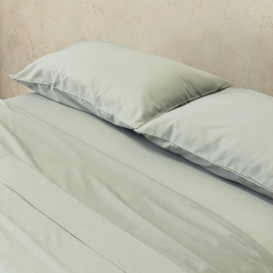Light grey bedspread and pillows on a bed against a beige wall.