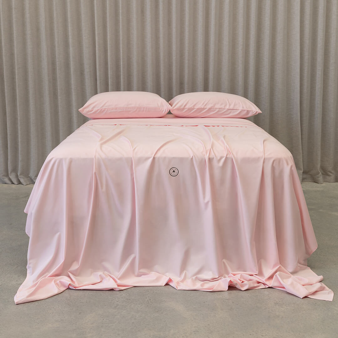 Soft pink bedding set on a bed, against a neutral background.