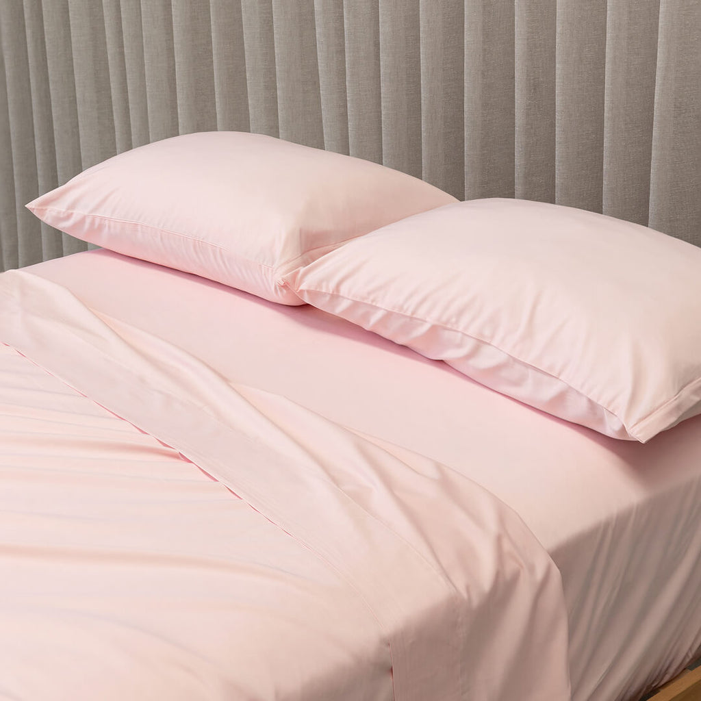 Pink bedding set with two pillows on a bed against a gray curtain background.