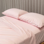 Pink bedding set with two pillows on a bed against a gray curtain background.