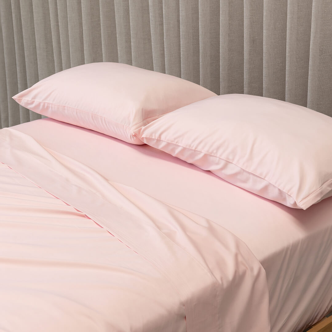 Pink bedding set with two pillows on a bed against a gray curtain background.