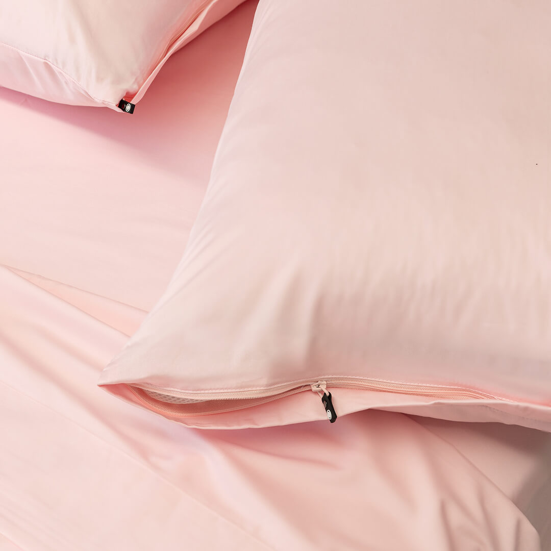 Close-up of two pink pillowcases with a zipper on a light pink background.