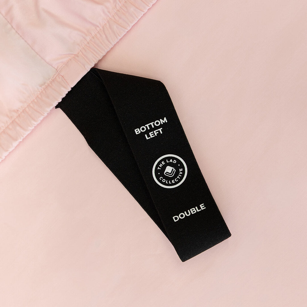 Black labelled corner loop strap on pink fitted sheet.