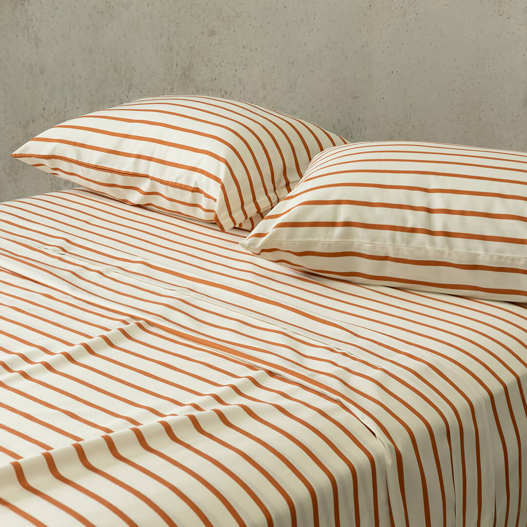Striped bed sheets and pillows on a bed with a neutral background.