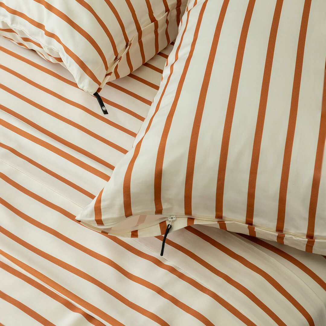 Close-up of striped bedding with orange and white stripes on a neutral background.