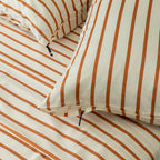 Close-up of striped bedding with orange and white stripes on a neutral background.