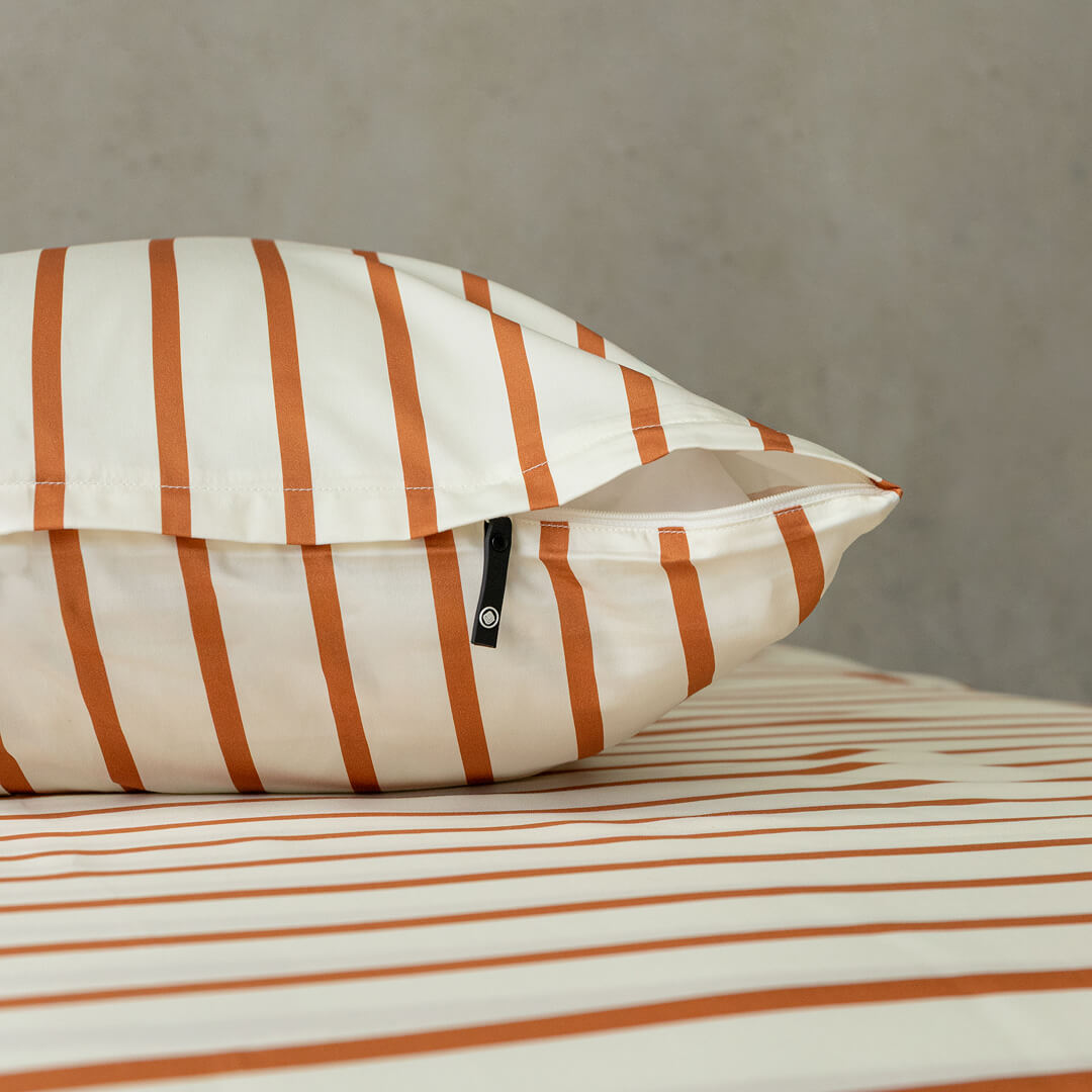 Striped pillow and duvet cover on a bed with a neutral background.
