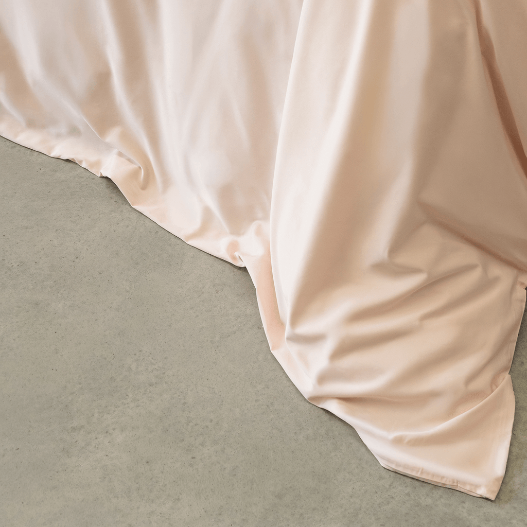 Detailed view of the blush pink quilt cover fabric draping naturally over the bed edge, showcasing its smooth feel and elegant flow.
