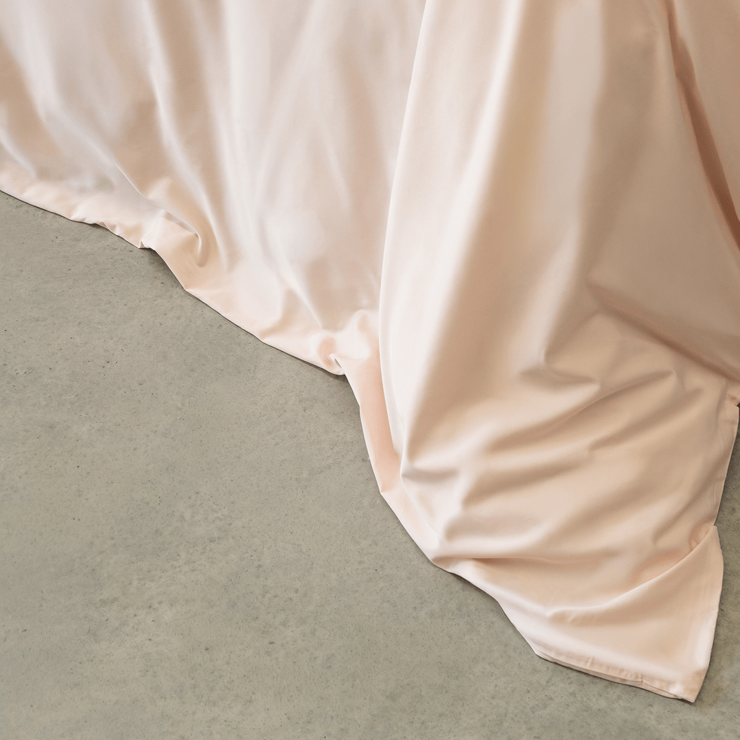 Detailed view of the blush pink quilt cover fabric draping naturally over the bed edge, showcasing its smooth feel and elegant flow.
