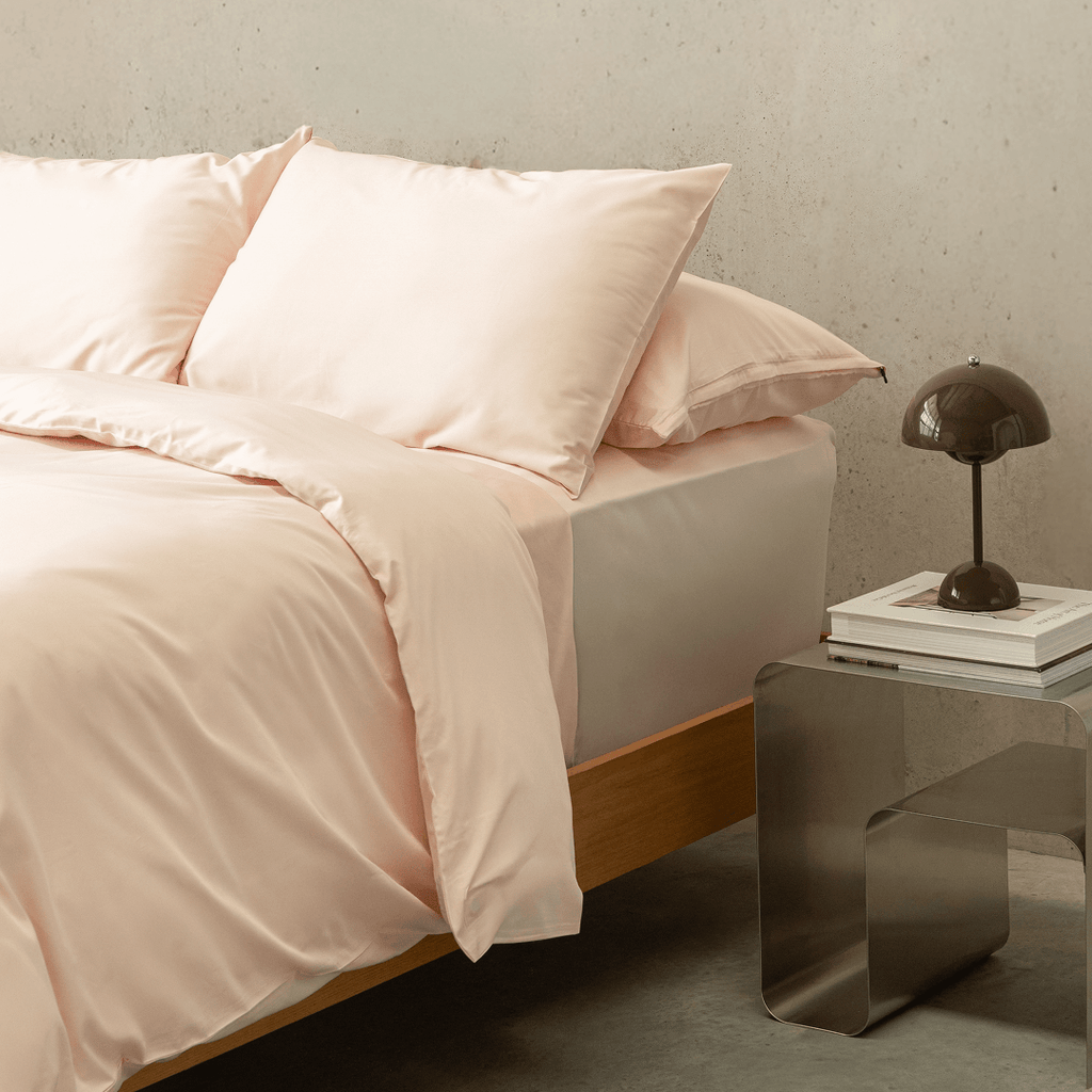 Angled bedroom scene featuring a blush pink quilt cover set with matching pillowcases, showcasing the bedding’s smooth drape and refined styling.
