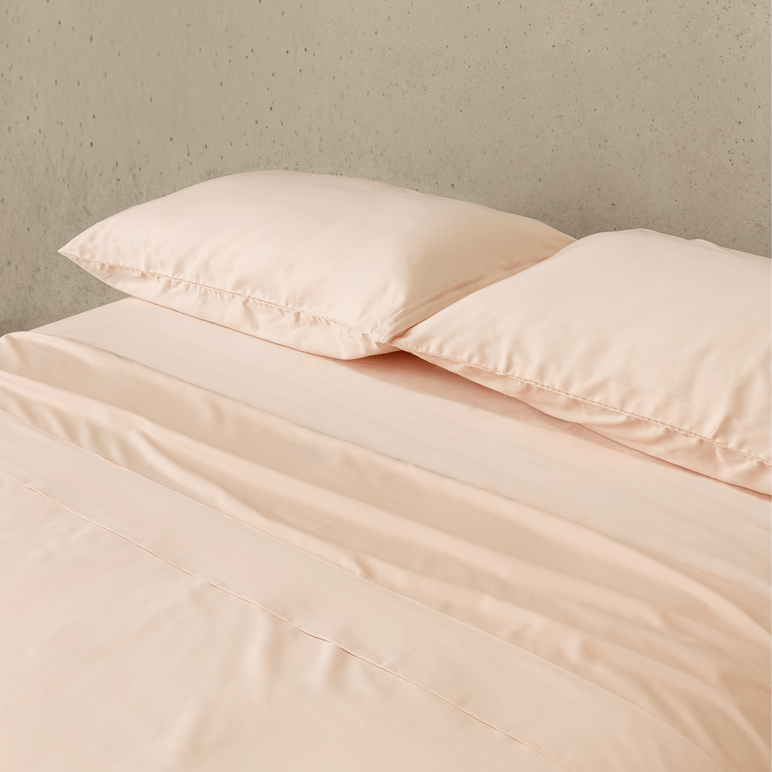 Close-up of blush pink fitted sheets and matching pillowcases, highlighting the soft-touch fabric, smooth texture, and refined appearance.