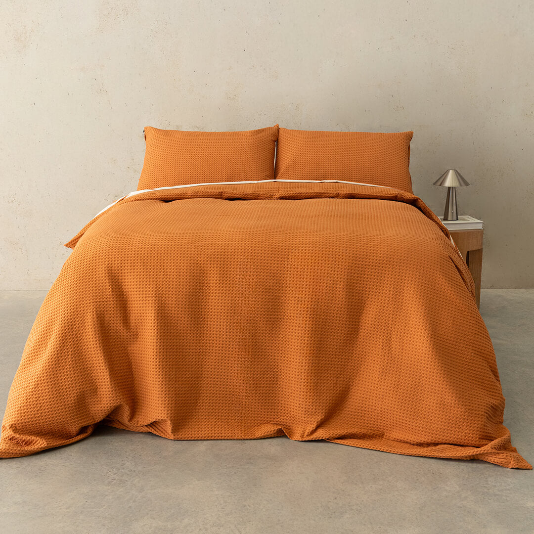 Orange quilted bedspread on a bed with matching pillows in a minimalistic room.