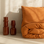 Orange textured pillow and two vases on a neutral background