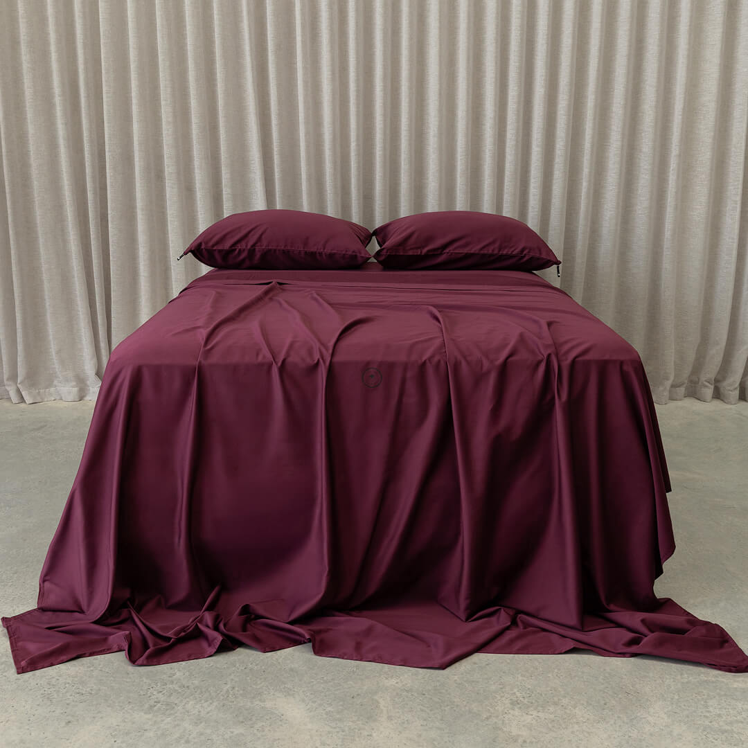 Burgundy bedspread and pillows on a bed against a beige curtain background