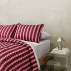 Close-up of burgundy and pale pink striped bedding layered over light-coloured sheets, with a metallic bedside lamp and stacked books.