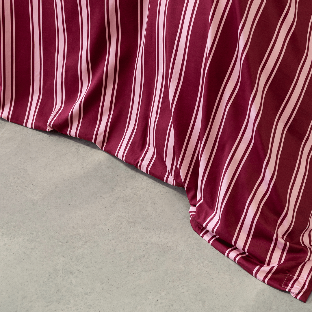 Close-up of a burgundy quilt cover with pale pink vertical stripes draping in soft folds onto a concrete floor.