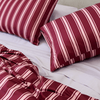 Two burgundy and pale pink striped pillows arranged on light-coloured sheets with the matching quilt cover gathered in front.