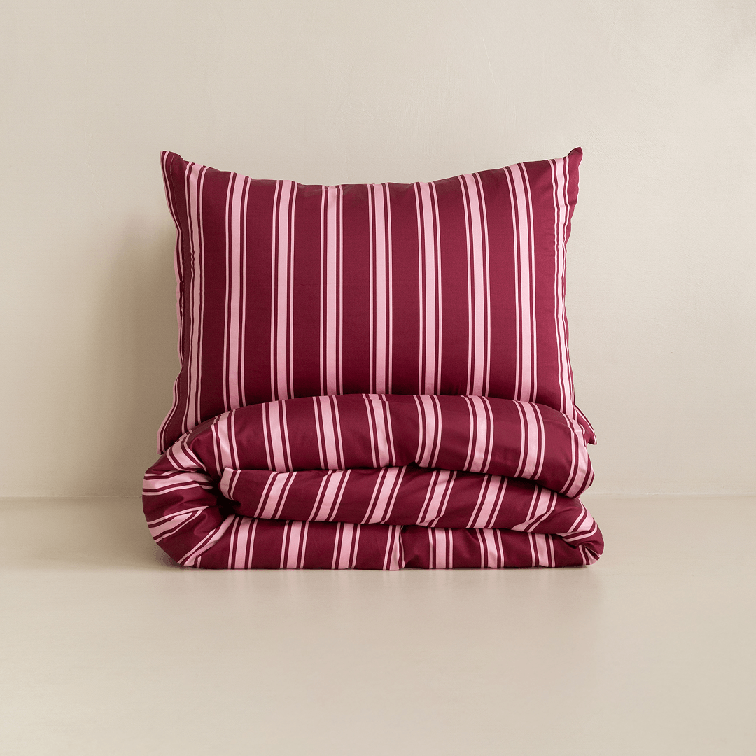 A burgundy and pale pink striped pillow displayed above a neatly folded matching quilt cover against a neutral background.