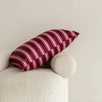 A burgundy and pale pink striped pillow resting diagonally on a cream textured armchair against a neutral wall.