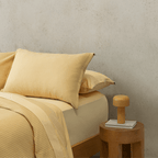 Side view of a yellow waffle-weave pillowcase resting on top of a smooth sheet on a styled bed