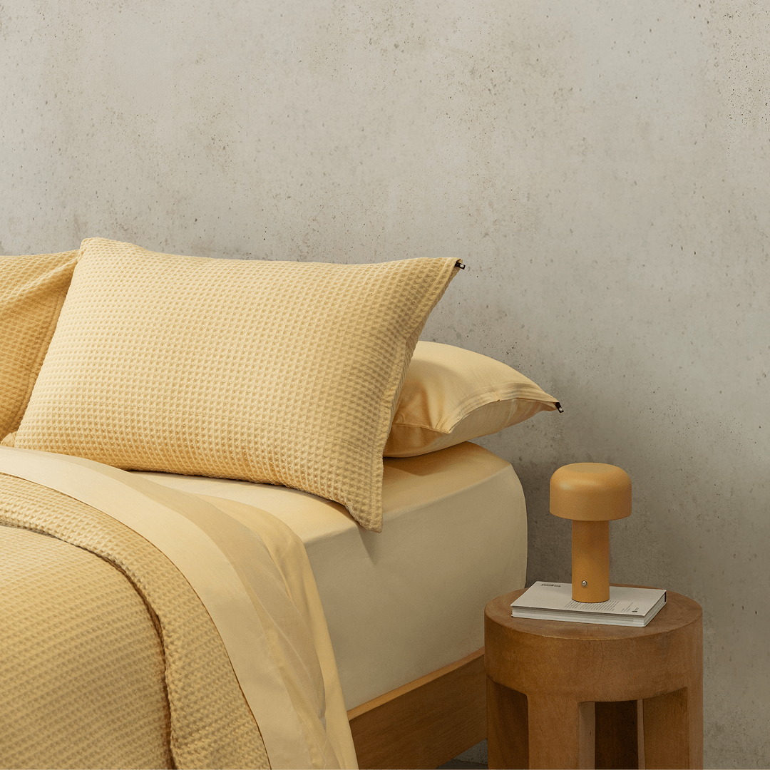 Side view of a yellow waffle-weave pillowcase resting on top of a smooth sheet on a styled bed