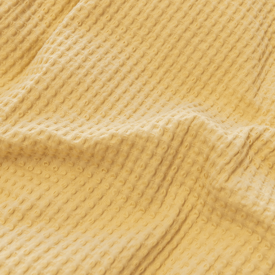 Extreme close-up showing the textured waffle-weave pattern and soft cotton fabric of the yellow quilt