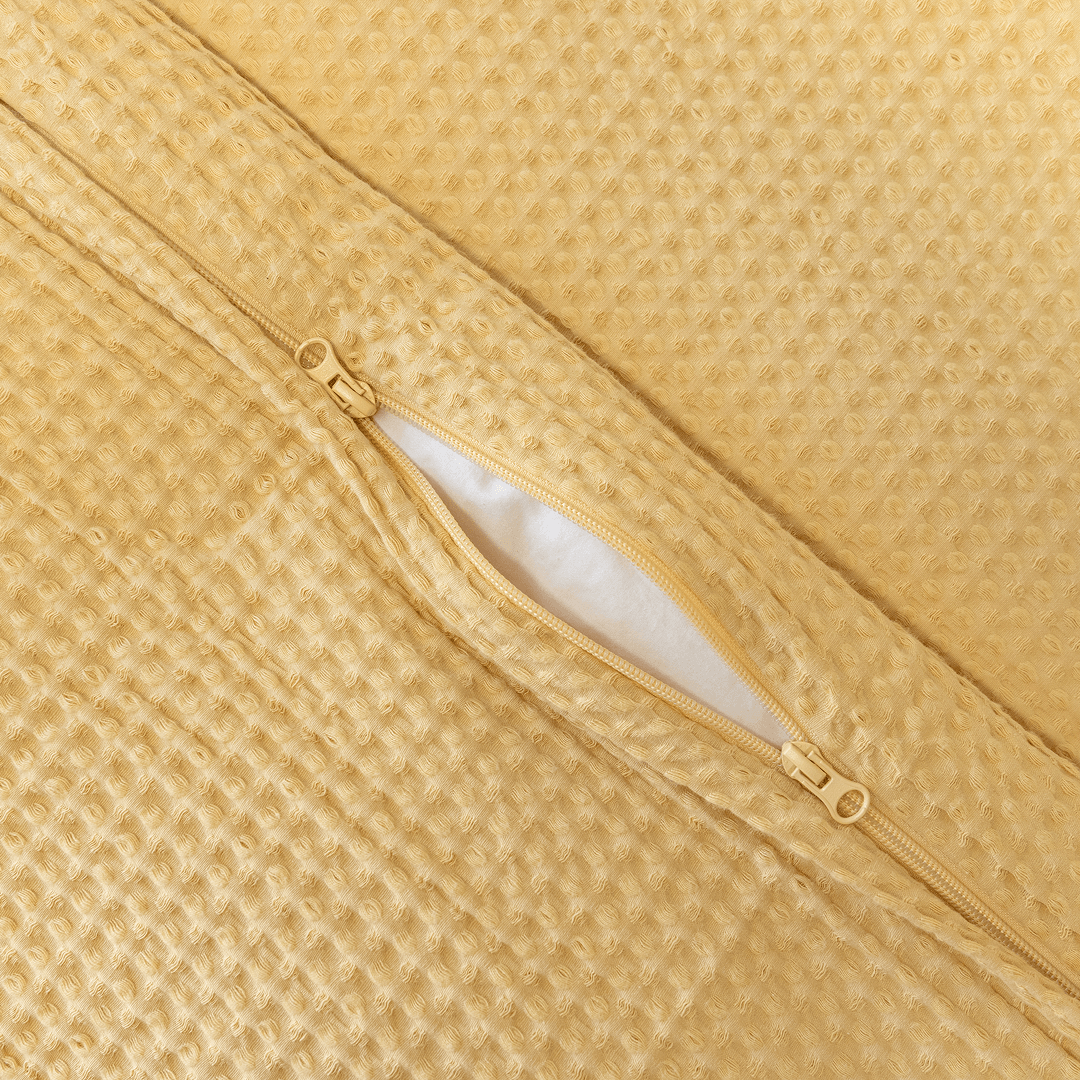 Close-up detail of a yellow waffle-weave quilt cover with an open zipper closure revealing white insert material