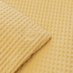 Close-up corner view of the yellow waffle-weave quilt fabric folded over to show the stitched edge