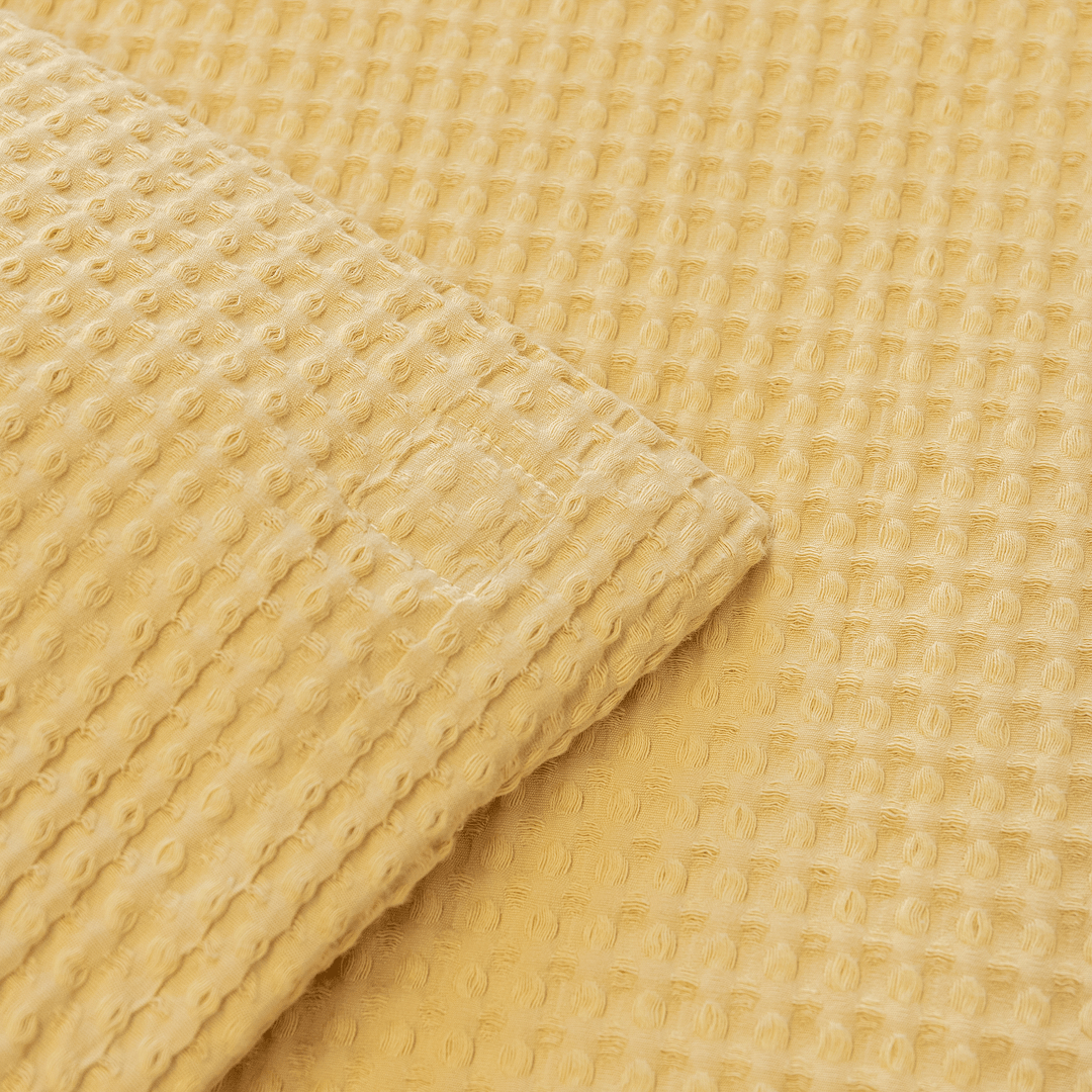 Close-up corner view of the yellow waffle-weave quilt fabric folded over to show the stitched edge