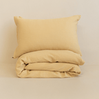 Neatly folded yellow waffle-weave quilt with one matching pillowcase placed on top against a neutral backdrop