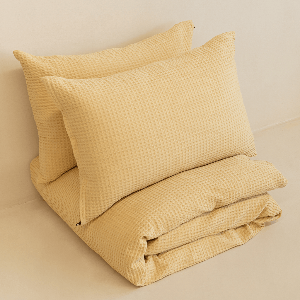 Neatly folded yellow waffle-weave quilt with two matching pillowcases stacked behind it