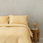 Styled bedroom view of yellow waffle-weave bedding next to a wooden nightstand and small bedside lamp