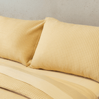 Close-up of two yellow waffle-weave pillowcases leaning against a smooth yellow flat sheet on a bed