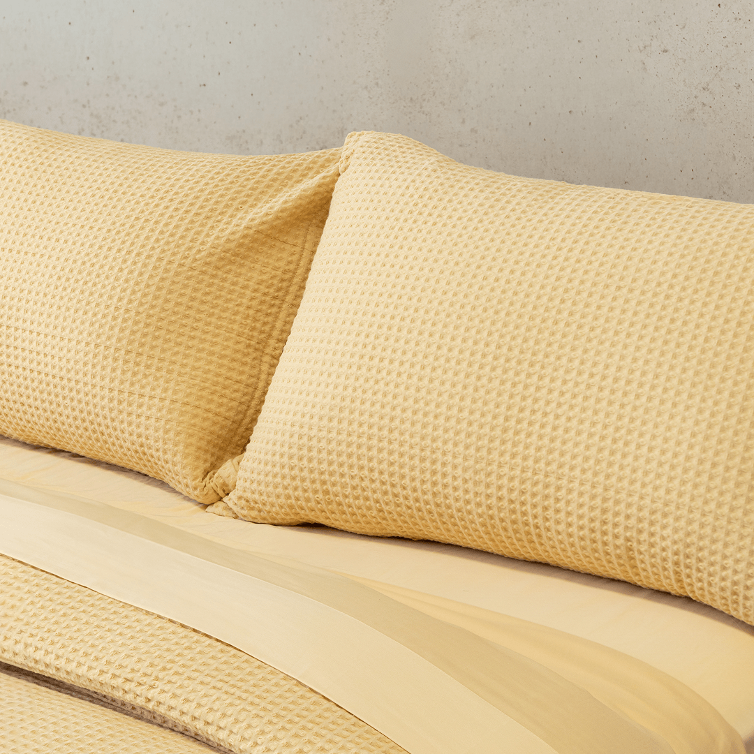 Close-up of two yellow waffle-weave pillowcases leaning against a smooth yellow flat sheet on a bed
