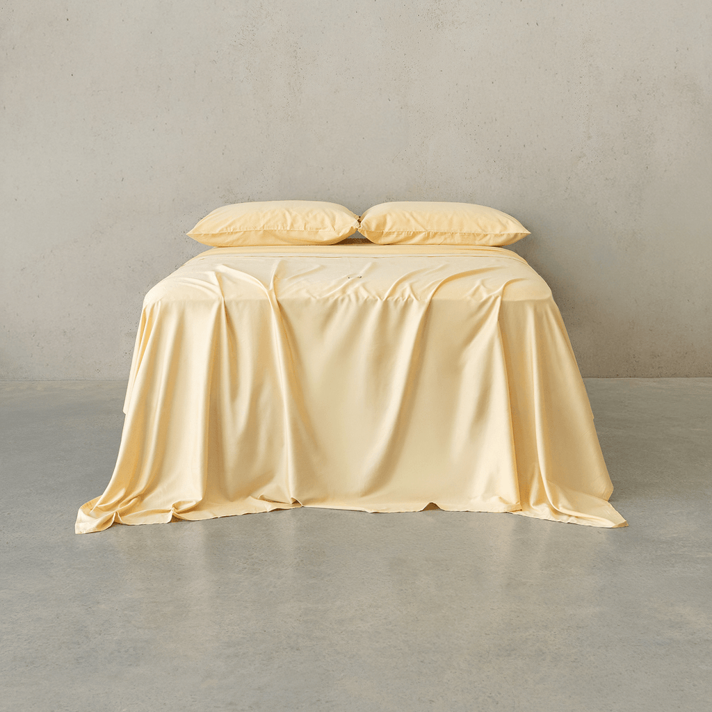 Pale yellow bed sheet set draped over a bed with two matching pillowcases against a neutral wall