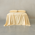 Pale yellow bed sheet set draped over a bed with two matching pillowcases against a neutral wall