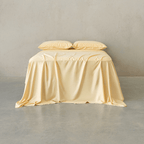 Pale yellow bed sheet set draped over a bed with two matching pillowcases against a neutral wall