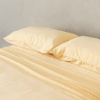 Angle view of two pale yellow pillowcases and matching flat sheet neatly arranged on a bed